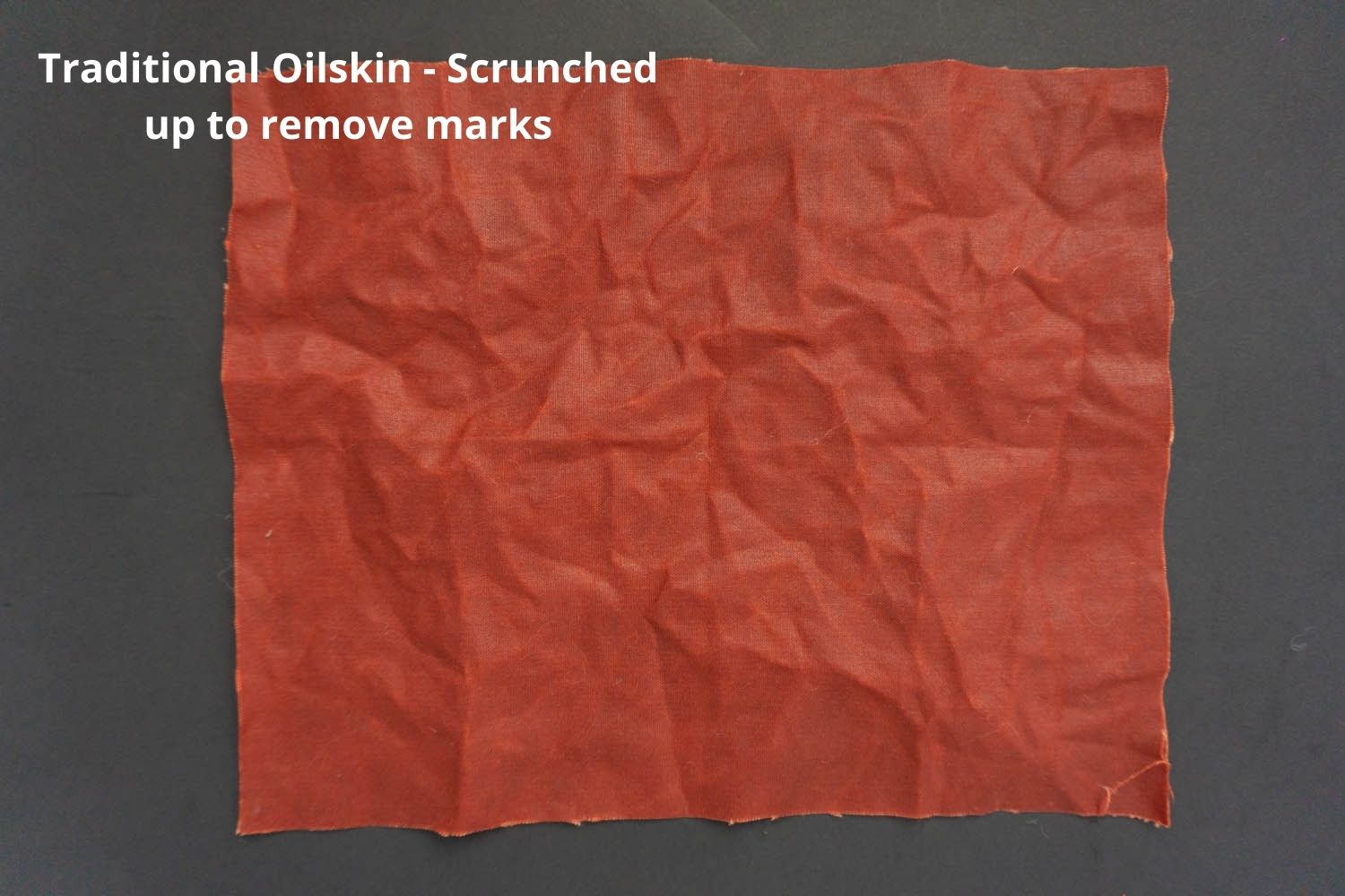 conker coloured traditional oilskin on a dark background that has been scrunched up 