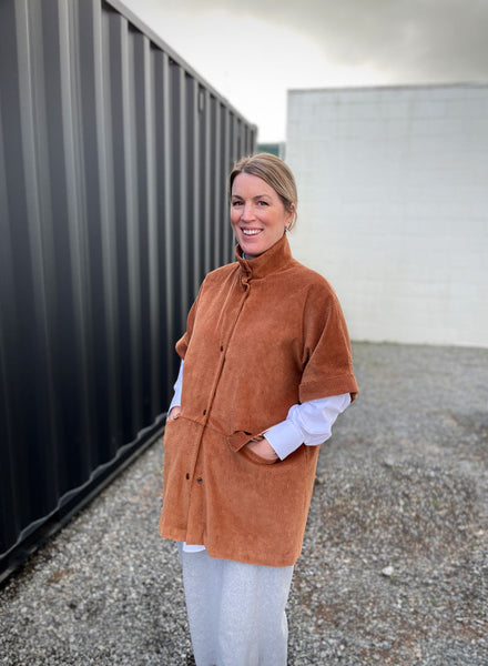 a white lady stood in front of a grey background wearing a toffee coloured corduroy jacket. 