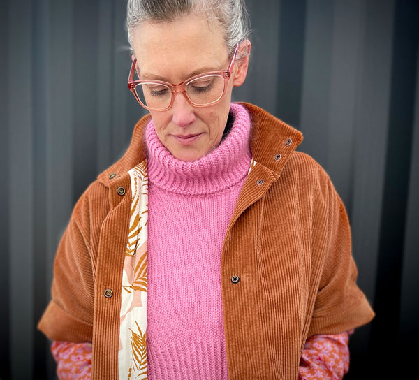 A white woman wearing a pink wool jumper and a toffee coloured cord jacket