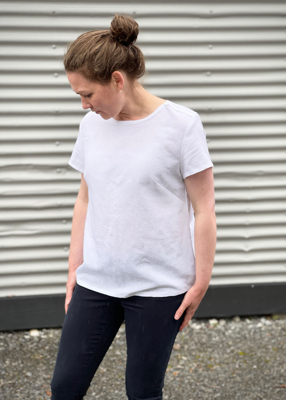 A white girl standing against a corrugated wall with a white t-shirt and black jeans