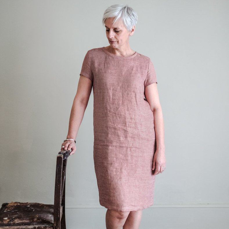 a white woman with white hair wearing a pink dress holding on to chair