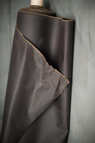 a photo of a roll of oilskin on a roll leaning up against a grey background. The fabric is slightly unravelling