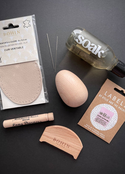 a selection of beige coloured items on a black background. There is a darning egg, labels, piling comb, darning needles and elbow patches