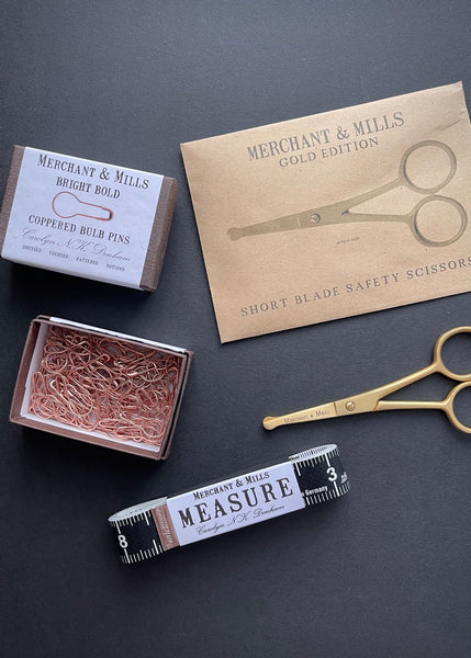 gold scissors, bronze bulb shaped pins and a black tape measure are on a black background