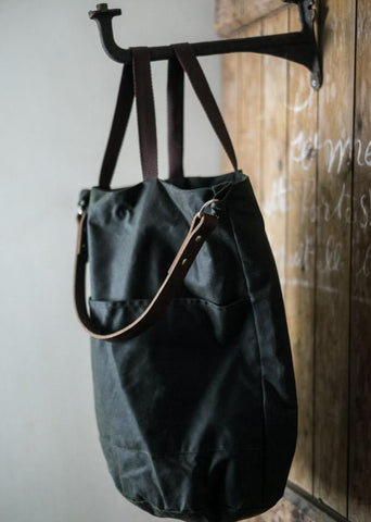 a black oilskin tote bag hanging on a black cast iron hook attached to a wooden wall