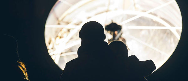 the outline of two people looking up at a massive light