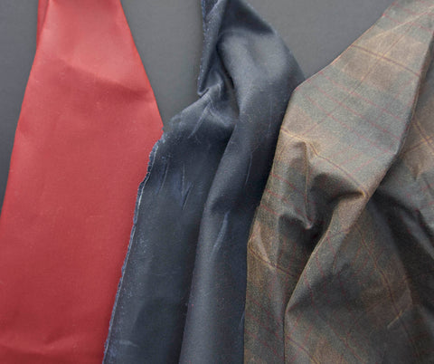 three oilskins draped over a black background from left to right the colours are deep red, black and brown