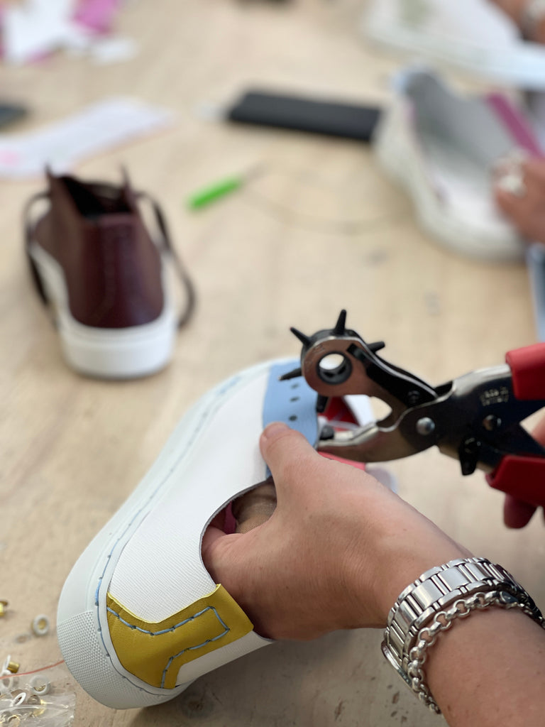 a close up of a white lady punching a hole in her trainers to create lace holes