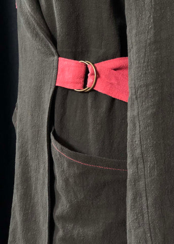 a close up of the belt of the Sienna makers jacket. it has two brass d rings and the pink belt is looped through them. It also shows some pink topstitching on the green pocket. 