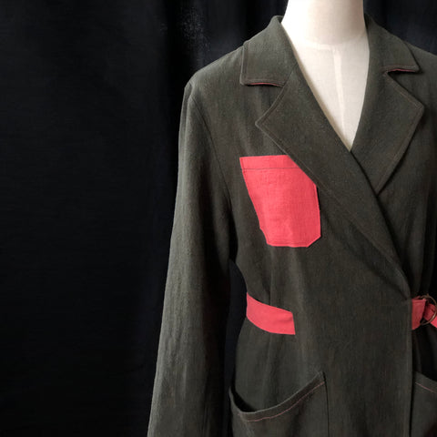 a picture of the Sienna maker jacket on a dressmakers bust. the green linen jacket has a salmon pink belt and pocket and shows off a lovely notched collar