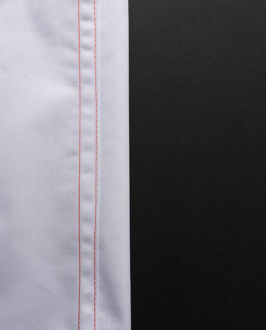 a white pice of fabric to the right hand side with orange flat felled stitch on the right hand edge with a black background