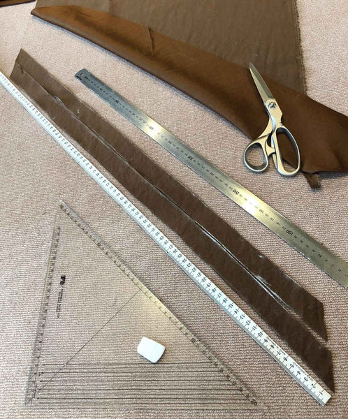 a photo of some strips of fabric on the floor with a large triangle ruler, large metal ruler and scissors