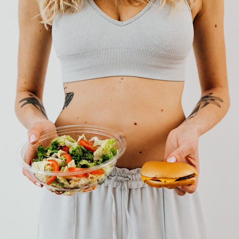 A woman holding an hamburguer and a salad trying to choose the best option
