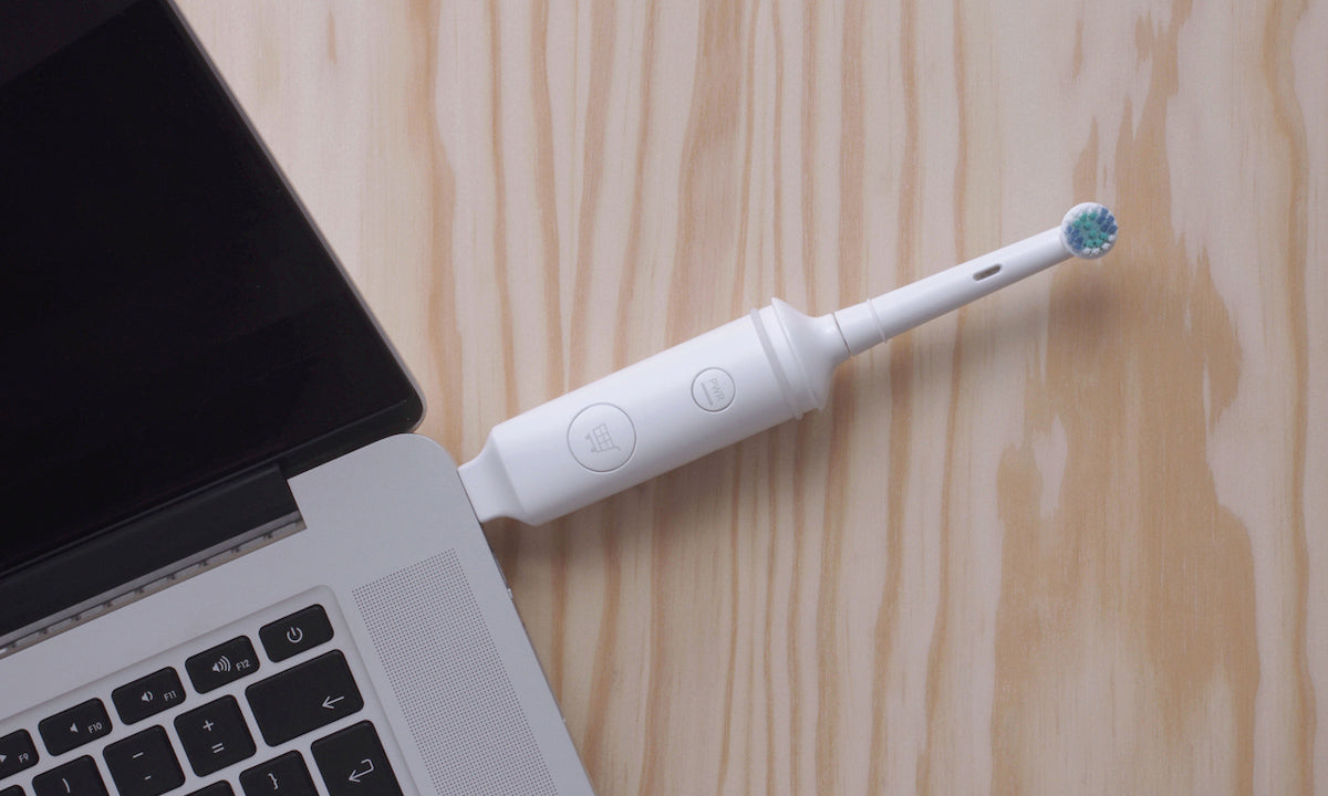 An electric toothbrush plugged into the USB port of a laptop.