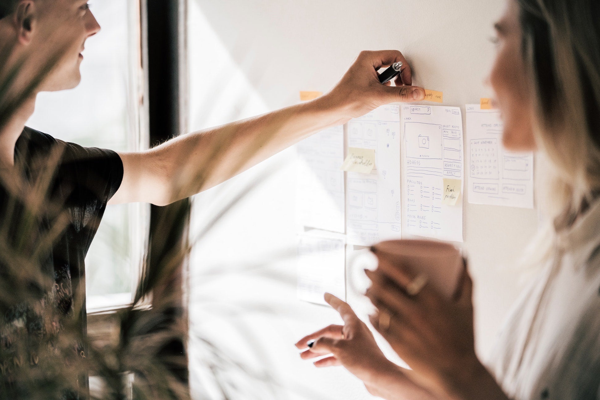 Two people putting papers on a whiteboard.