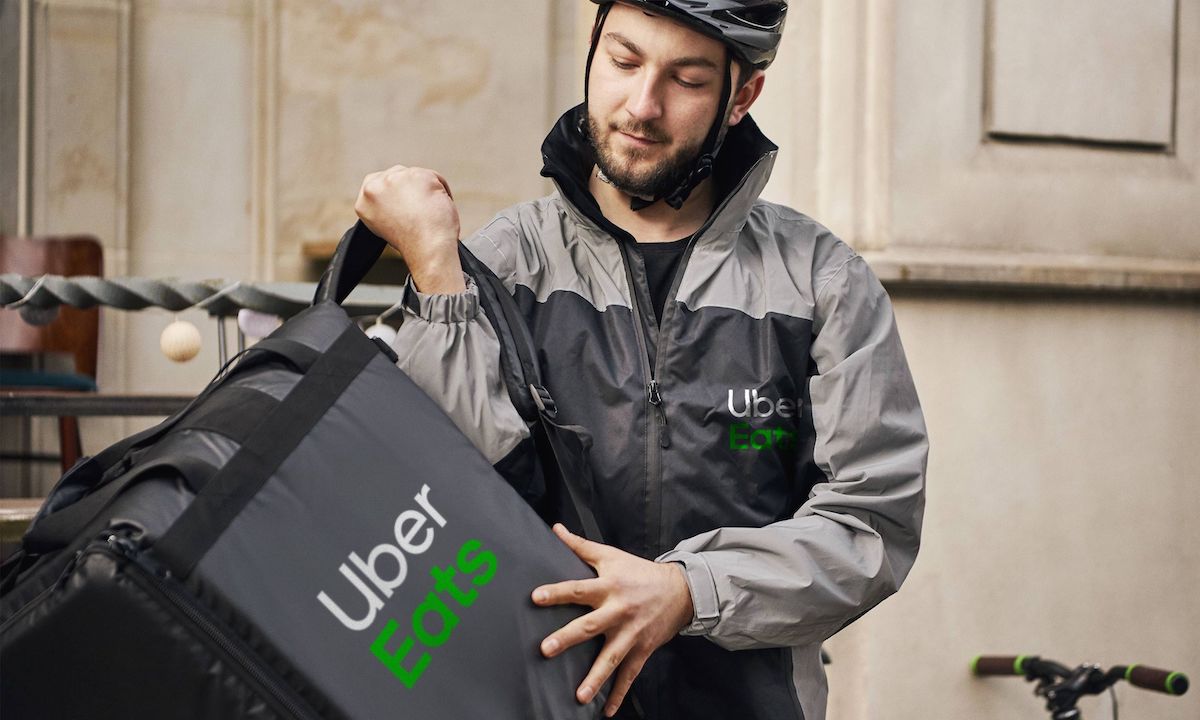 Person with a helmet and jacket holding a food delivery bag.