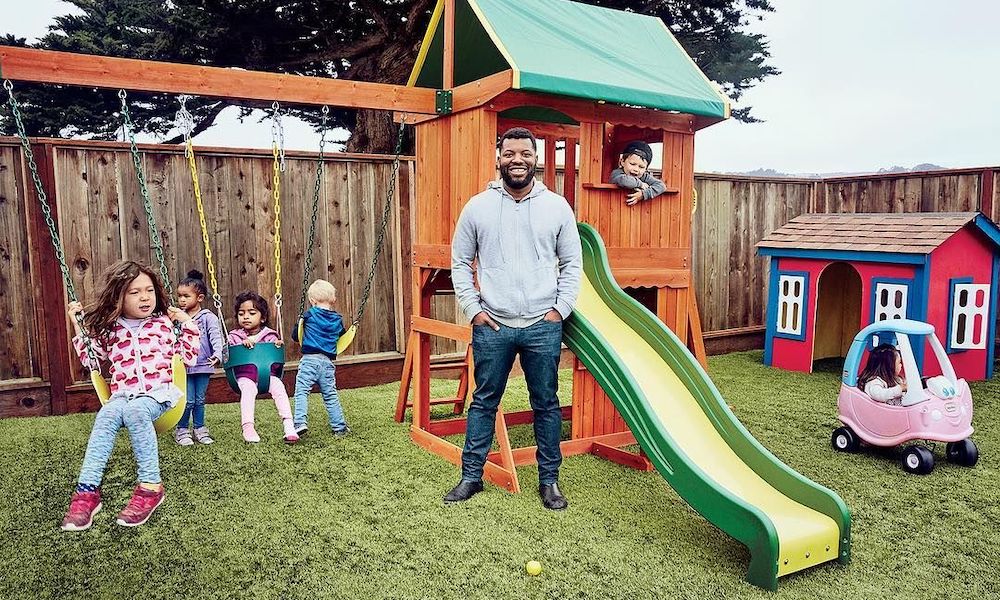 Wonderschool CEO and Co-founder Chris Bennett stands outside in front of a playset while children play.