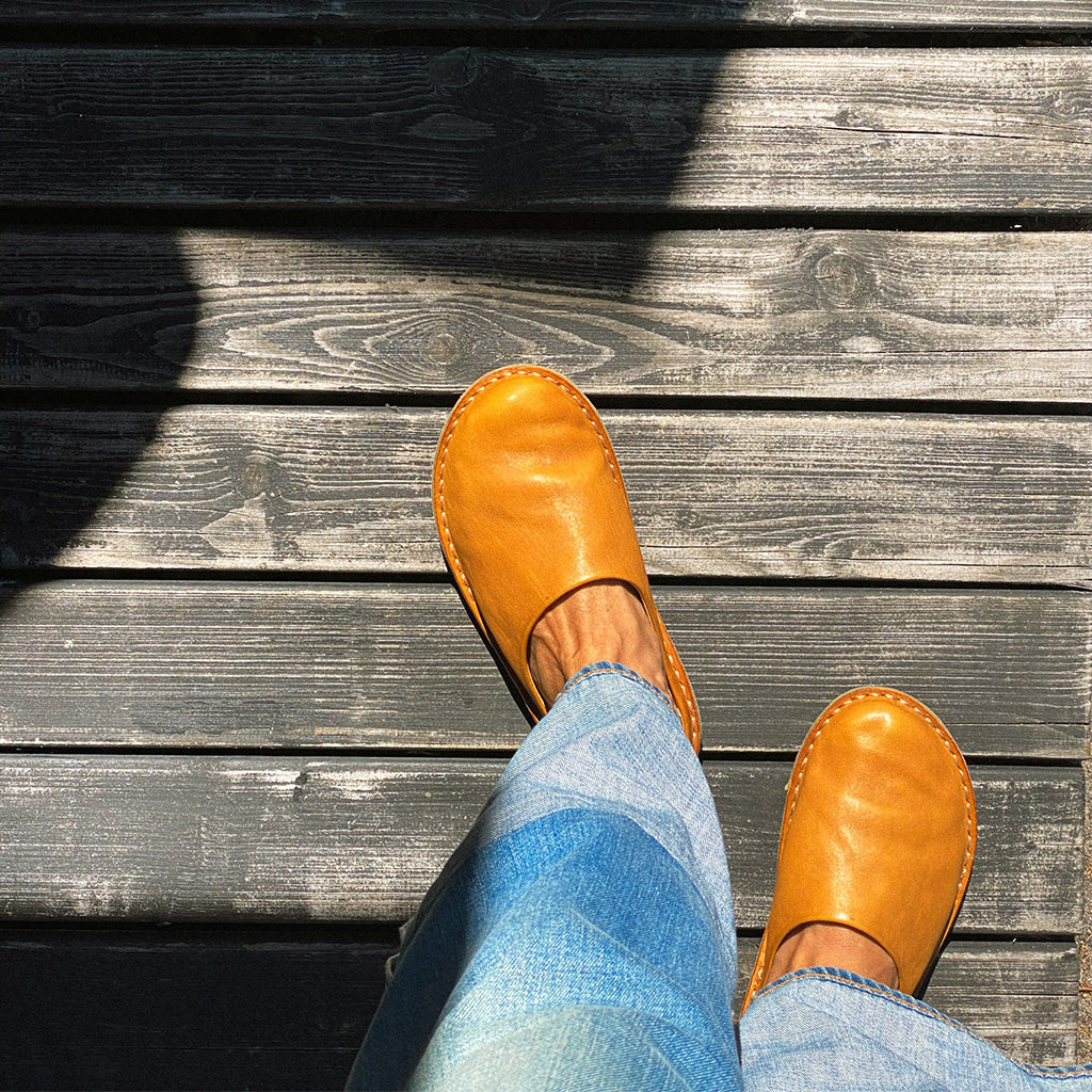 Person wearing tan shoes and blue jeans standing on wooden flooring.