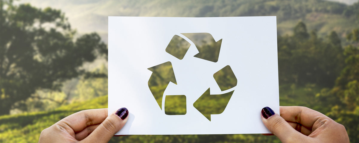 A piece of paper held up in front of a landscape with the recycling symbol cut out of it
