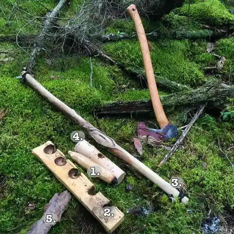 A group of wood sticks and an axe placed on a mossy forest floor.