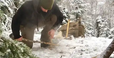 A bushcrafter igniting a fire with two sticks in the snow.
