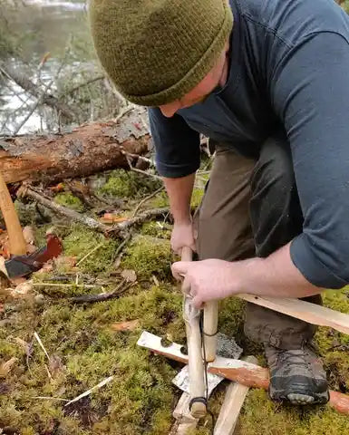 A bushcrafter igniting fire with two carved sticks and rope.