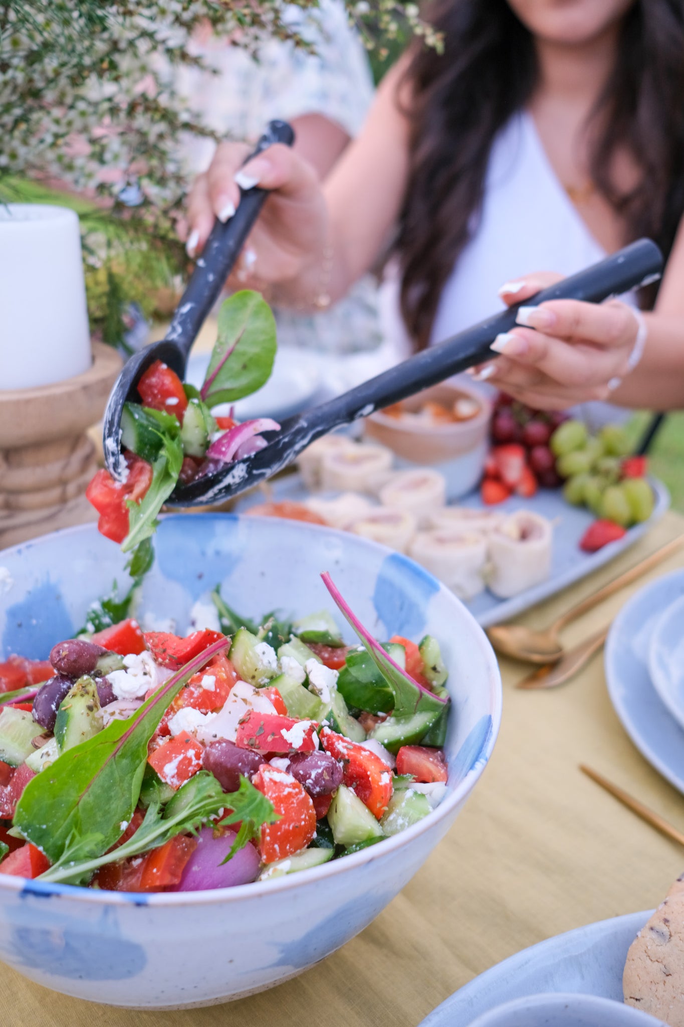 Woman serving a Greek Salad by Soul Origin Catering in a handmade blue and white stoneware bowl by Palinopsia ceramics