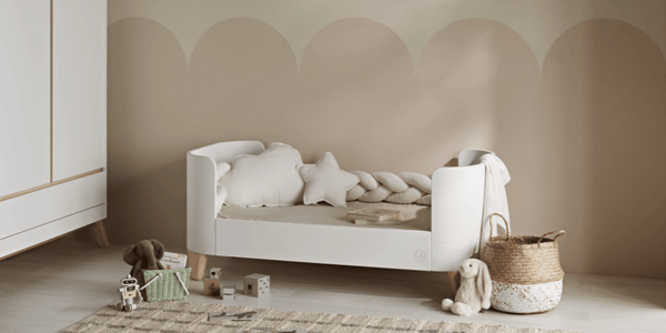 This image shows the braided pillow on the Serena First Bed Mode, the soft white decorative pillow set and the Soft White Muslin Blanket draped over the end of the bed. The Hera wardrobe is to the left of the image.