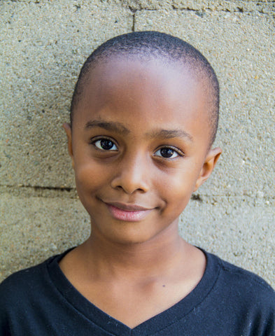 Young black boy next to a wall smiling