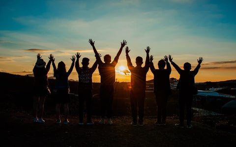 seven people holding their hands up in front of a sunset