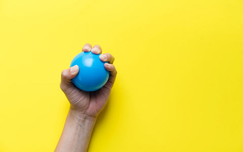 hand squeezing blue stress ball on yellow background