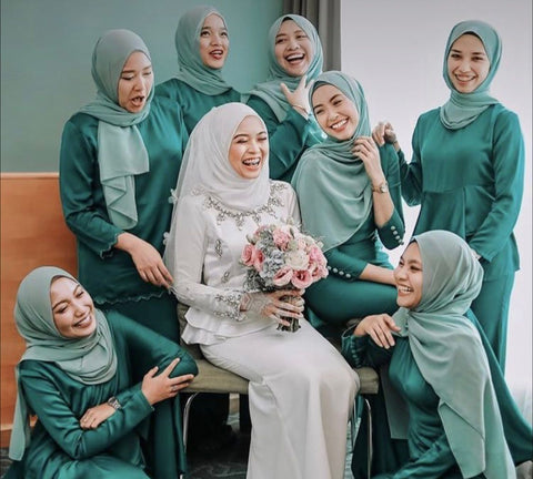 Bridesmaids wearing emerald green moira kurung sitting together with the bride.