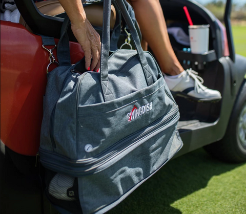 Grey bag on the side of a red golf cart with womans hand, leg and drink in background- SwingDish Bring It Bag - 