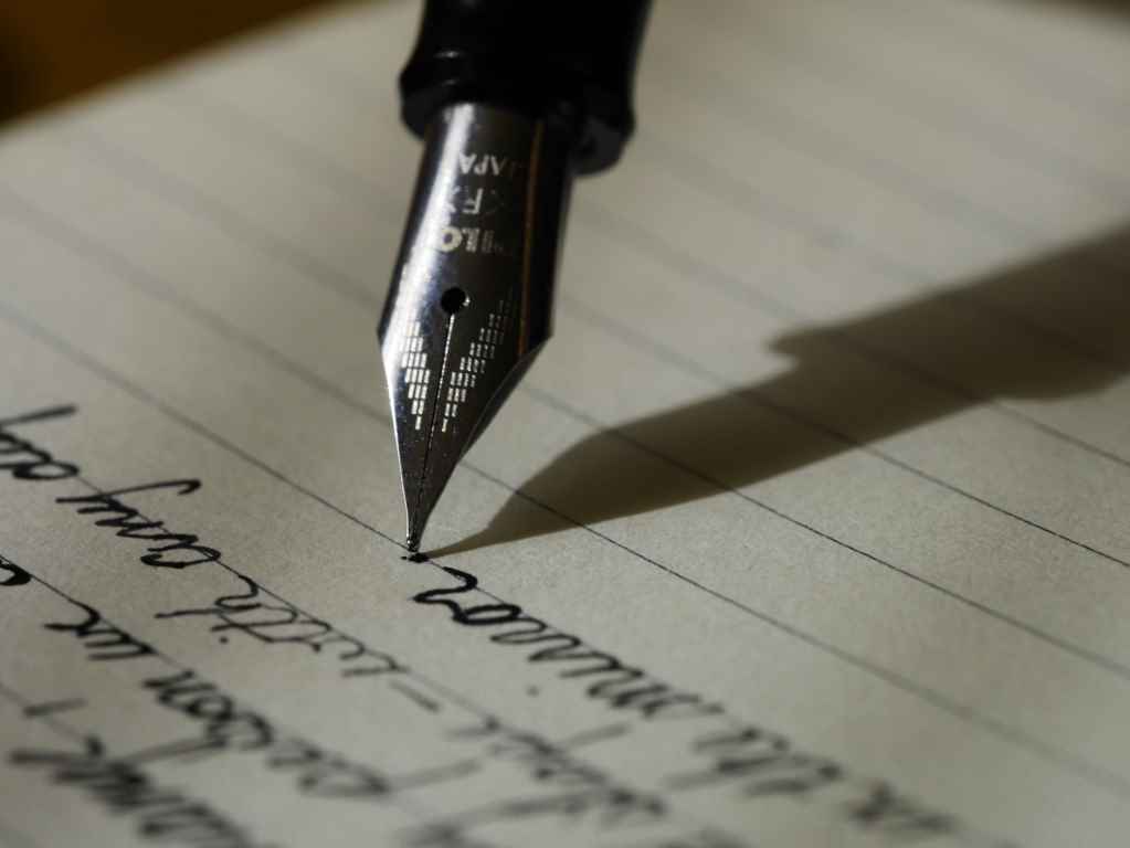Closeup image of a nib pen writing on a lined page. Photo by Aaron Burden.