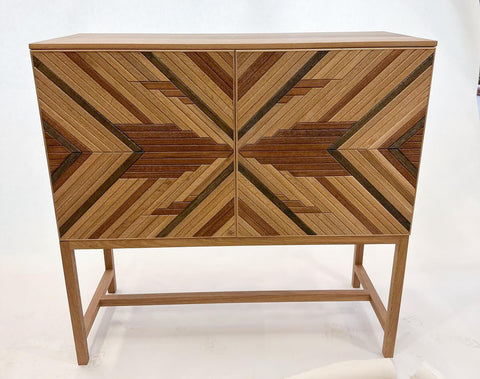 A white oak cabinet featuring a multi-colored wood mosaic on the door fronts.