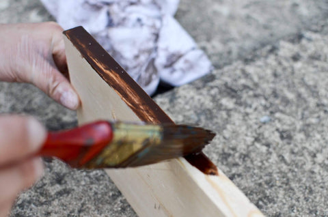 A hand showing how to apply wood stain colors to a piece of interior pine wood