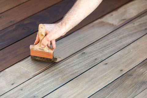 Applying a natural wood stain to a deck with a paint brush
