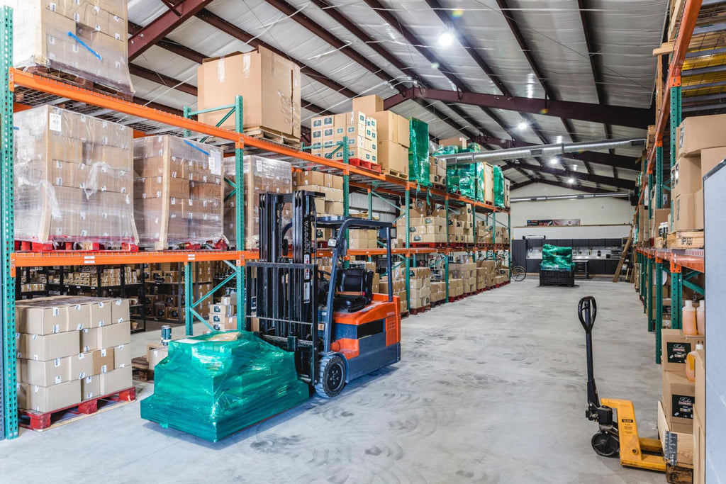 Forklift in stocked warehouse carrying a pallet.
