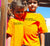 A girl and boy outside, with their arms around each other, wearing orange short sleeve t shirts.  Design in black.  Graphic of two statements.  Think flexibly, Think alternatively.