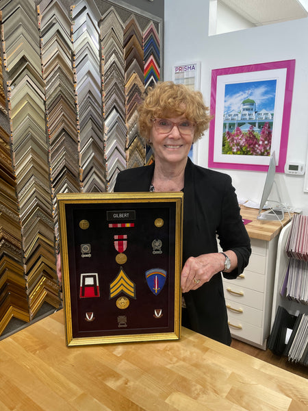 Sue Gilbert standing by the shadowbox of her husband's military memorabilia.