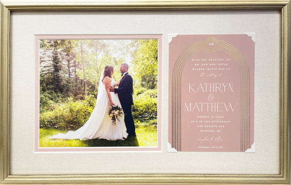 A photograph of a bride and groom captured majestically against a natural outdoor setting paired with their blush pink Art Deco wedding invitation are set inside a blush inner mat and shimmering fabric outer mat, with a delicate gold frame to match the arch on the invitation.