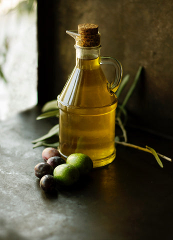 Olivenöl in Glasamphore mit Oliven davor auf Holztisch
