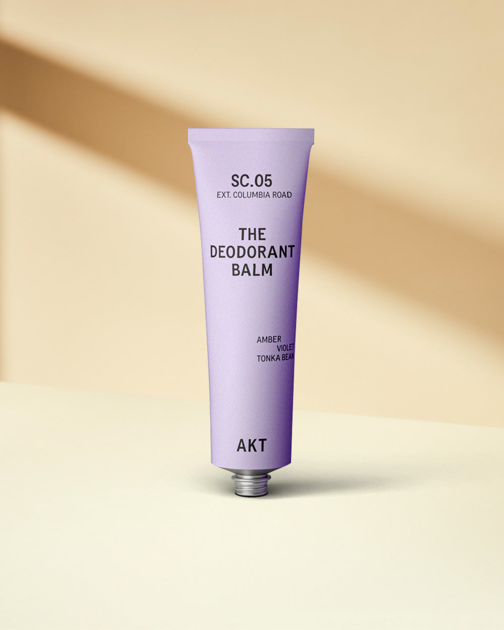 A purple tube of AKT deodorant balm against a beige background with a shadow.