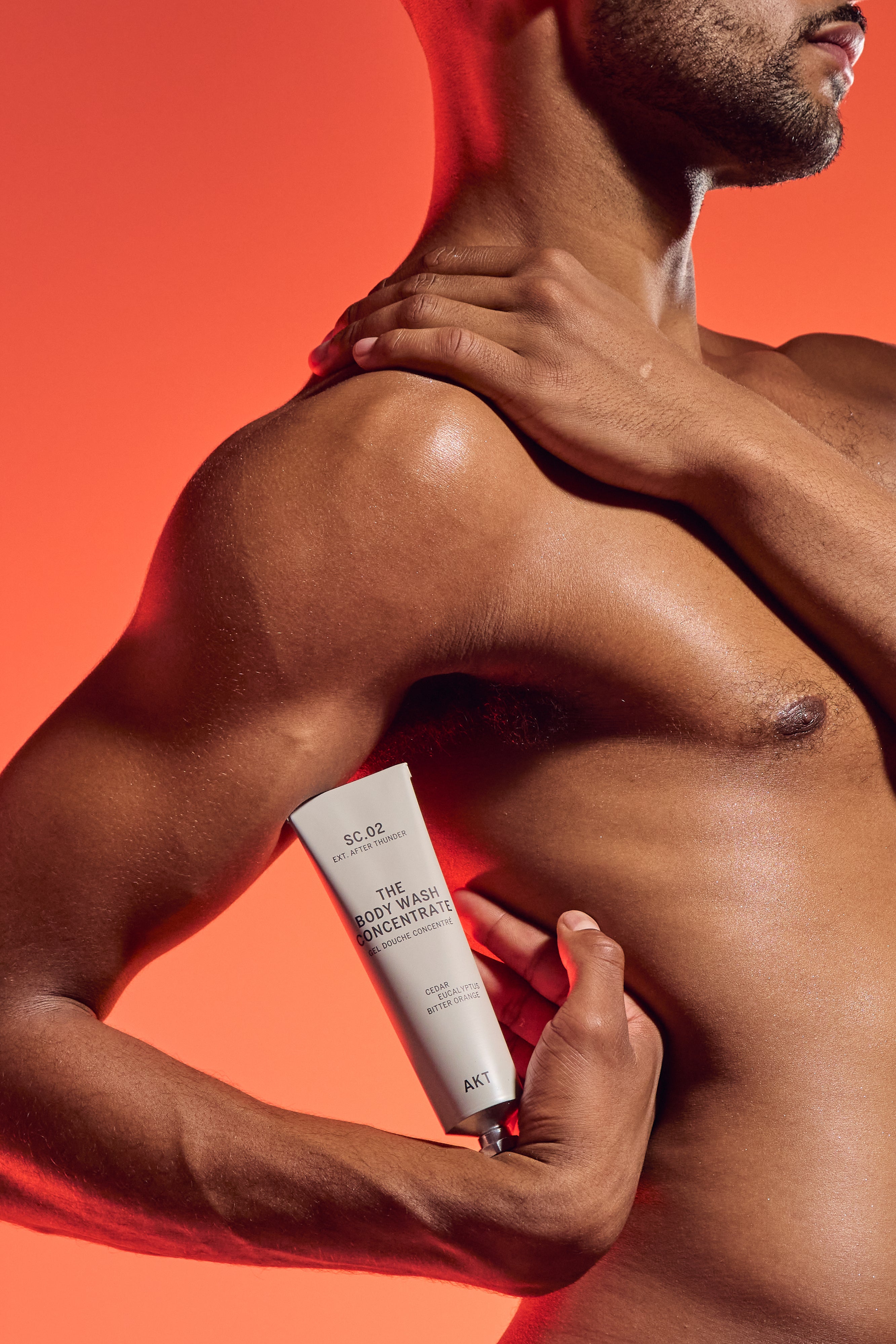 Man holding a tube of body wash concentrate against an orange background.