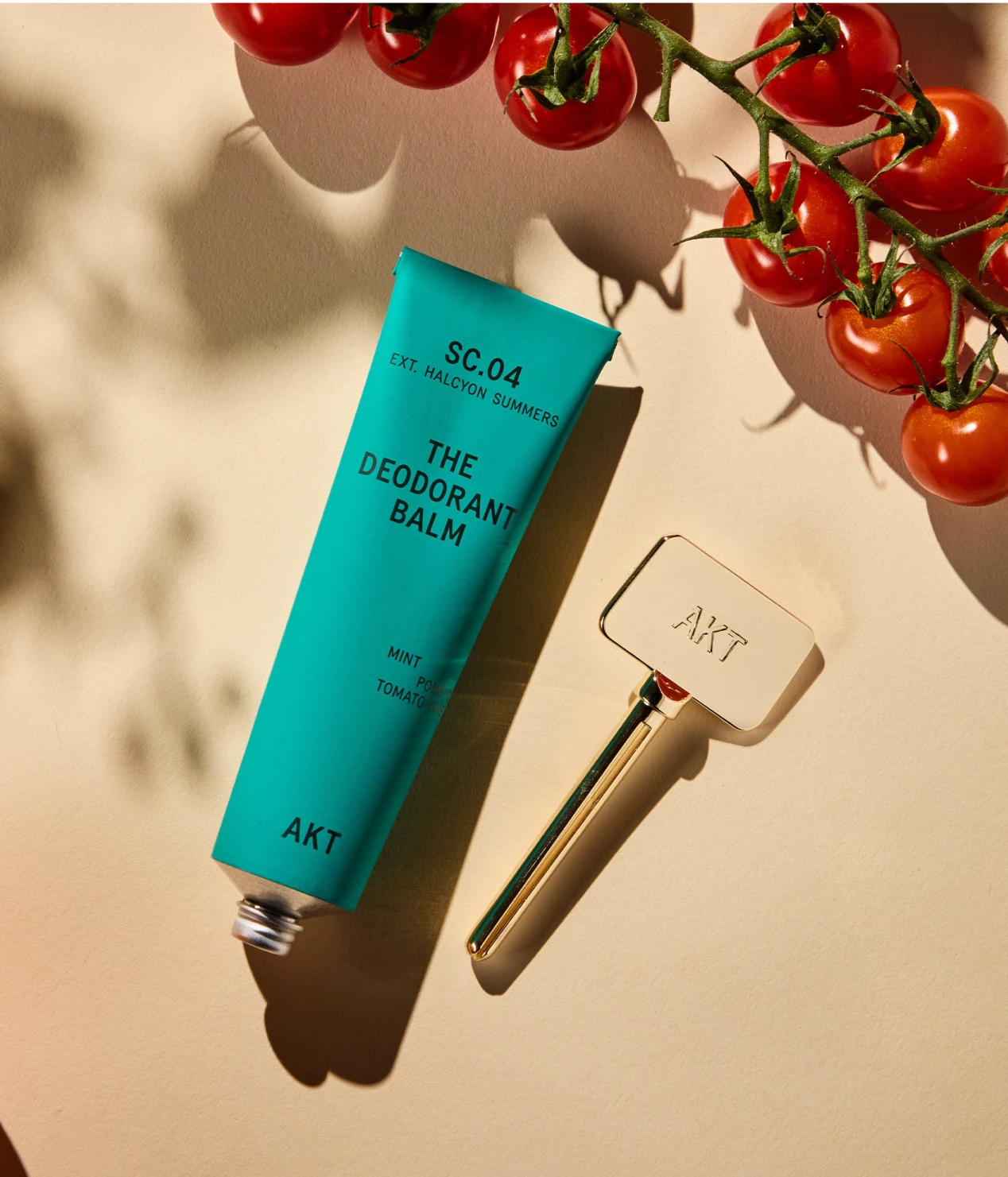 Deodorant balm tube with gold applicator next to cherry tomatoes on a branch.
