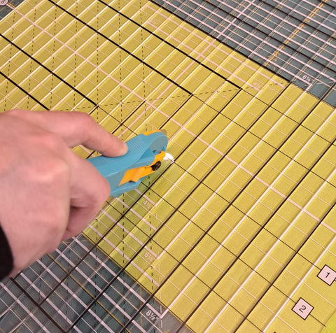 Quilter's hand using a rotary blade to cut yardage using the stripology ruler.