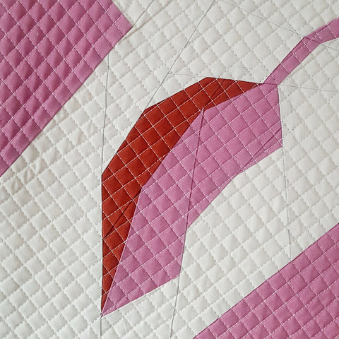 A foundation paper pieced leaf in pink and brown and quilted with a narrow square grid.
