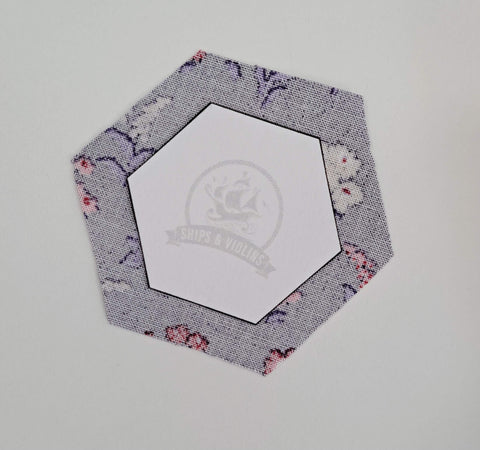 Paper hexagon template placed in the centre of fabric hexagon.