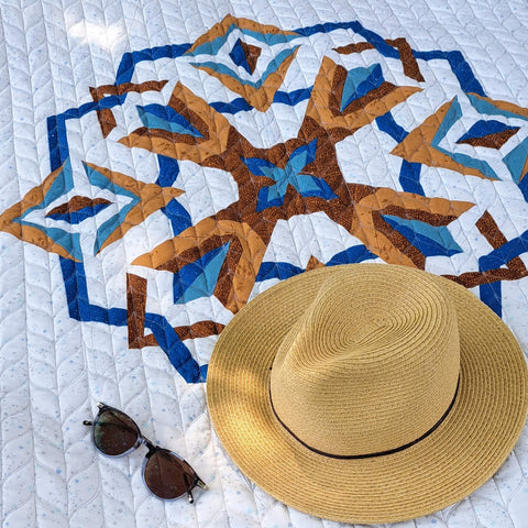 Nesting Phoenix quilt with hat and sunglasses resting on top.