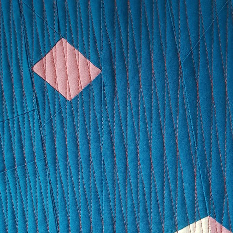 A pink foundation paper pieced abstract blossom on a navy background and quilted with a long diamond grid.